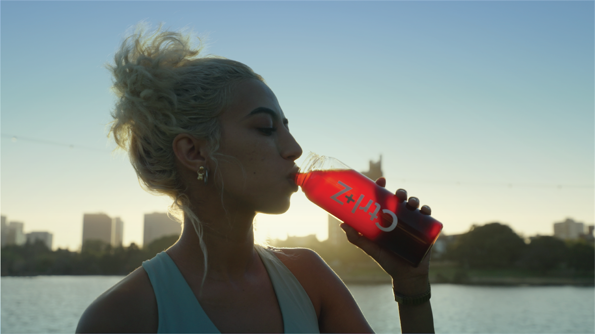 A woman in a city finishing a run at dawn is drinking a shaker bottle with Ctrl-Z in it.